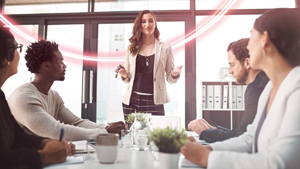 A group of men and women listening to a woman explaining something in an office space