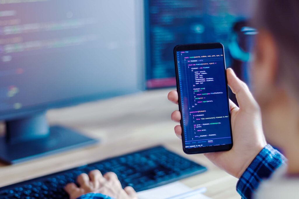 A person holding a phone with a code on a screen while looking at a computer screen