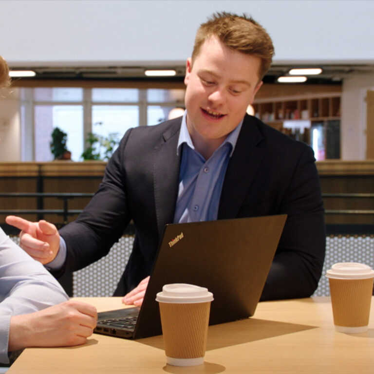 Devoteam's values: Frankness - a man talking to another person over a coffee and looking at a laptop